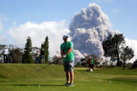 Sean Bezecny, 46, of Houston, Texas, takes a golf swing as ash erupts from the Halemaumau Crater near of the Kilauea Volcano in Hawaii, May 19. REUTERS/Terray Sylvester