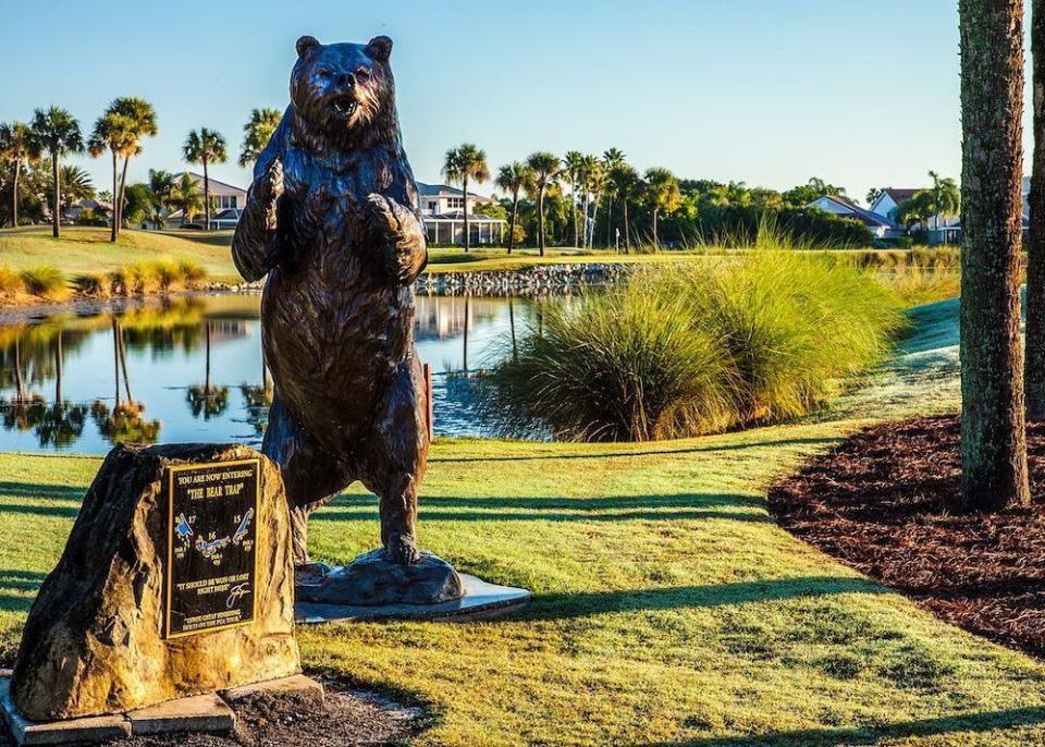 a statue of a bear by a pond on a golf course