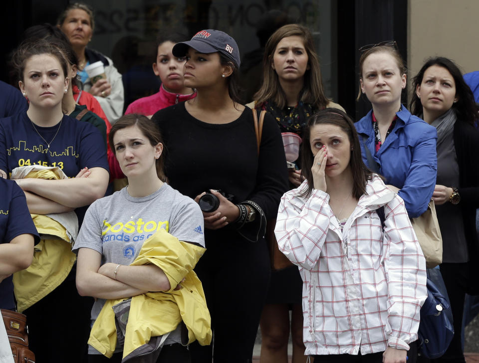 Heather McDade, of Boston, right, reacts while watching a tribute ceremony with others on an over-sized outdoor monitor, Monday, April 14, 2014, on Boylston Street, in Boston. The ceremony is being held for those killed and injured in the bombings at the finish line of the Boston Marathon a year ago. (AP Photo/Steven Senne)