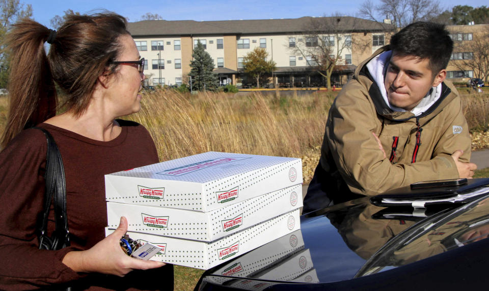 In this Saturday, Oct. 26, 2019 photo, Catherine Newton, left, buys three boxes of Krispy Kreme doughnuts from Jayson Gonzalez in Little Canada, Minn. Gonzalez, a Minnesota college student, says Krispy Kreme has told him to stop making doughnut runs to Iowa. Gonzalez told the Pioneer Press he was told his sales created a liability for the North Carolina-based company.  (Deanna Weniger/Pioneer Press via AP)