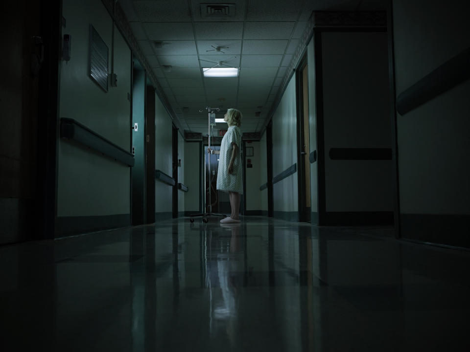 Person in a hospital gown standing in a dimly lit corridor, creating a mood of solitude