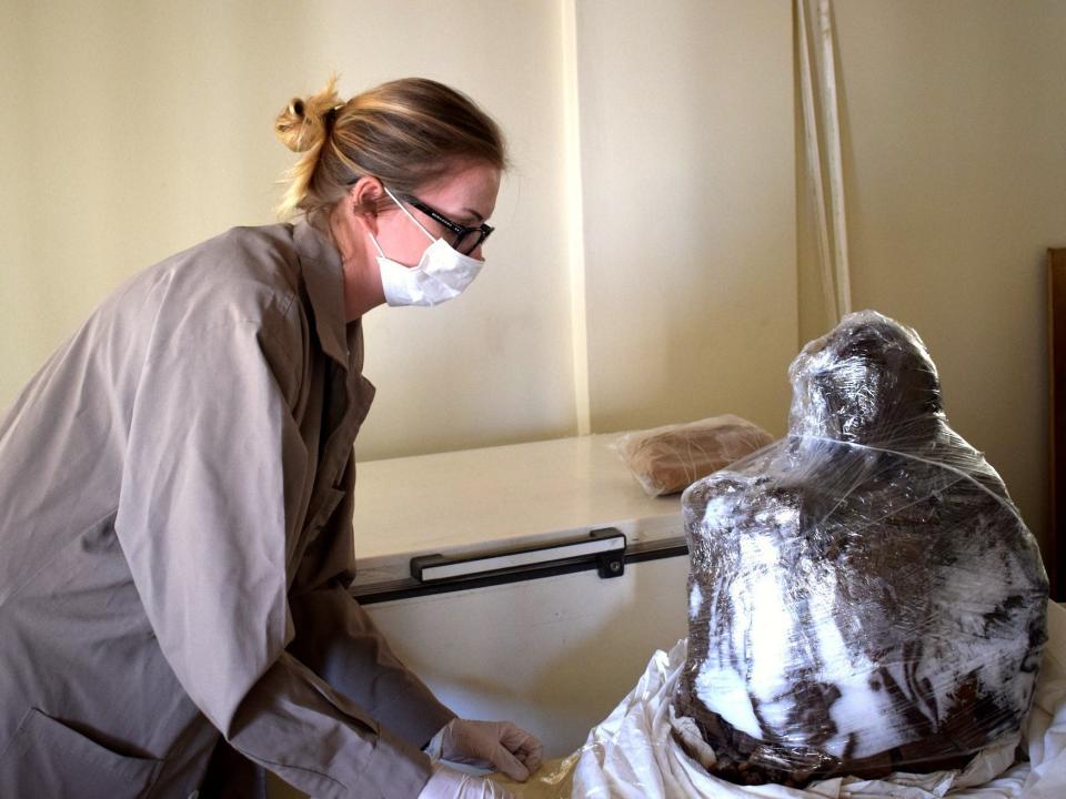 Dagmara Socha is wearing a lab coat as she examine remains of the Inca mummy wrapped in plastic.