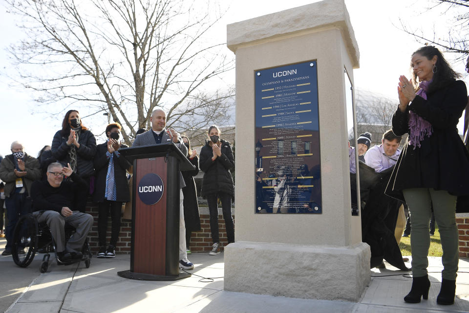 Former UConn Olympians watch as a monument commemorating people with a UConn connection who have competed in the Olympic games is unveiled on campus, Sunday, Dec. 5, 2021, in Storrs, Conn. Andy Bessette is at front left. Rebecca Lobo is just to the left of the monument. Asjha Jones is just to the left of the podium. (AP Photo/Jessica Hill)