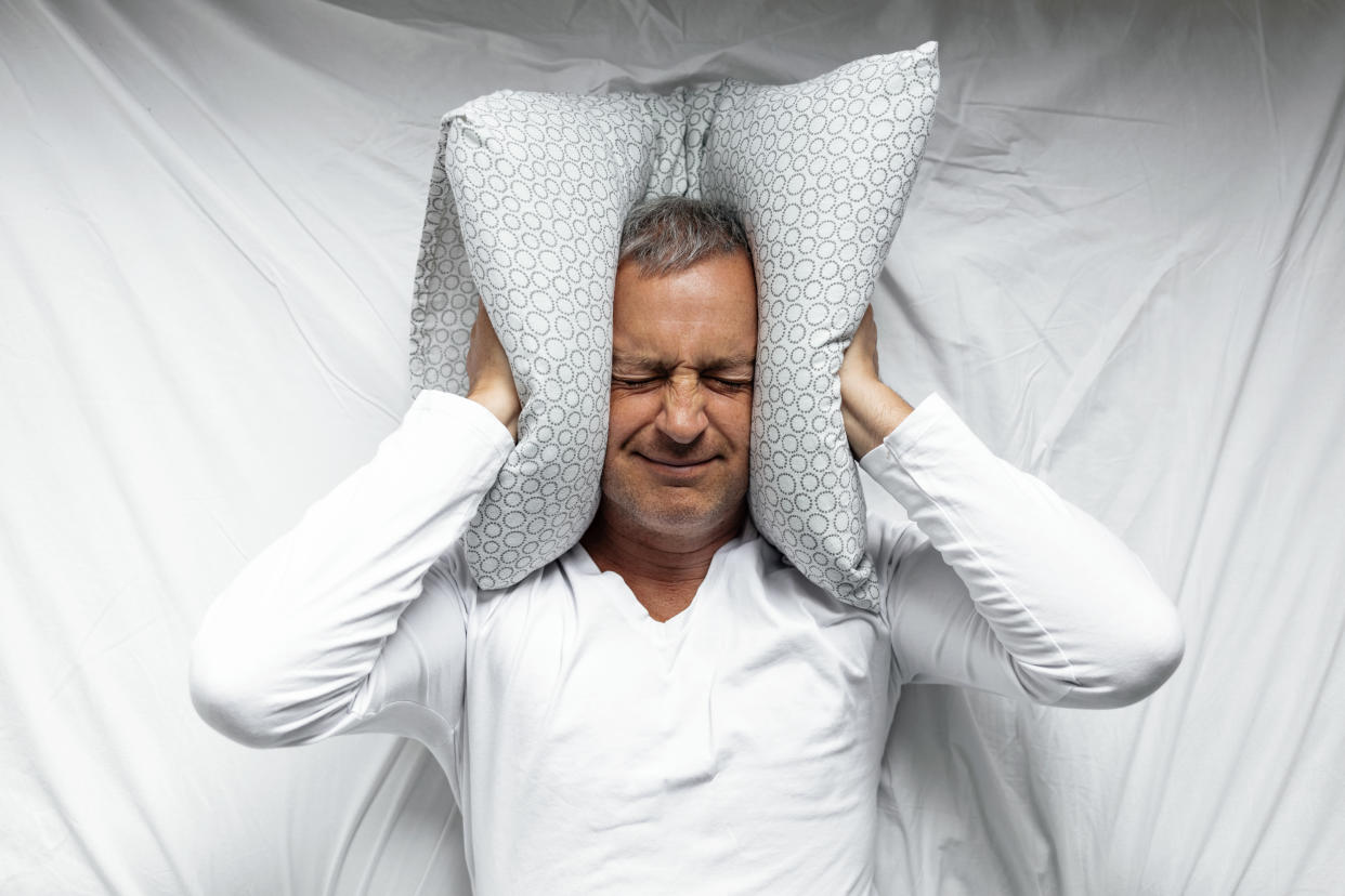 One mature man trying to sleep covering his ears to avoid neighbor noise at home or hotel during the day. 