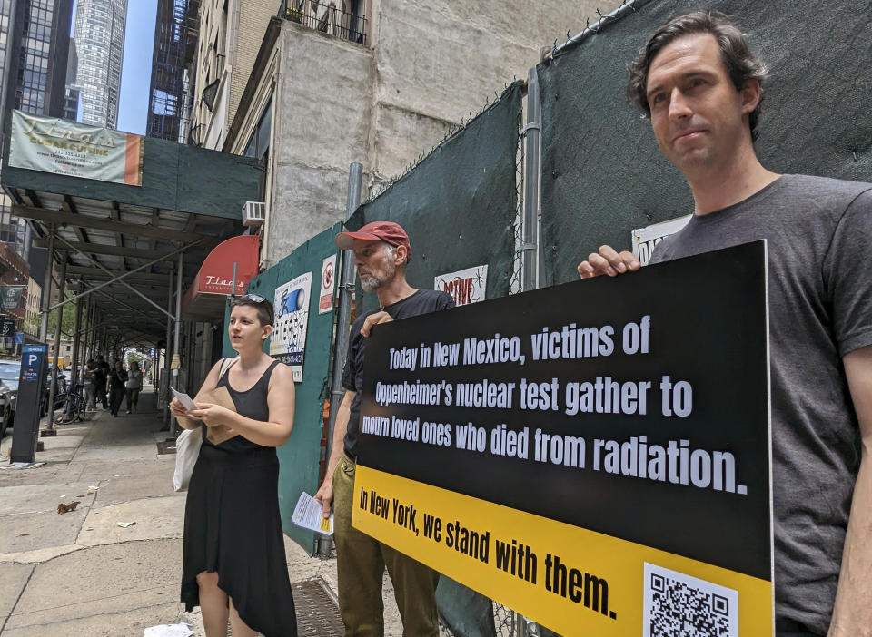 Matthew Bolton, a la derecha, y Jan-Christoph Zoels, al centro, sostienen un cartel mientras se manifiestan en la ciudad de Nueva York el 15 de julio de 2023. Activistas se reunieron para llamar la atención hacia los residentes de Nuevo México que estuvieron expuestos a la radiación durante la prueba atómica Trinity realizada en 1945 como parte del Proyecto Manhattan. El mitin procedió a una proyección y un panel de discusión sobre la nueva película "Oppenheimer". (Andrew Facini vía AP)