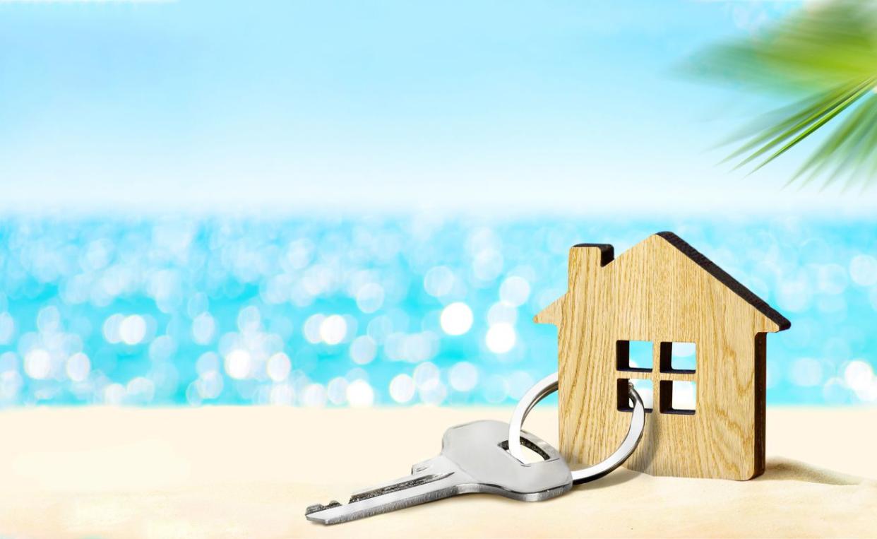 An image of a mini house with a key attached on a sunny beach.