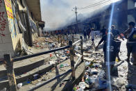 People walk through the looted streets of Chinatown in Honiara, Solomon Islands, Friday, Nov. 26, 2021. Solomon Islands Prime Minister Manasseh Sogavare on Friday blamed foreign interference over his government’s decision to switch alliances from Taiwan to Beijing for anti-government protests, arson and looting that have ravaged the capital Honiara in recent days. (AP Photo/Piringi Charley)