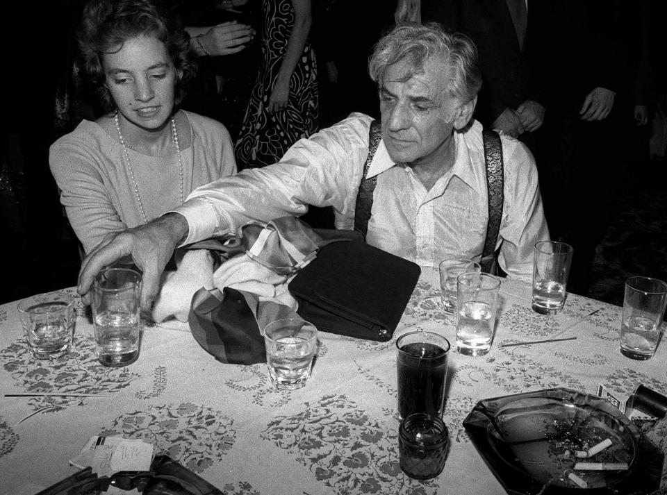 Conductor/composer Leonard Bernstein reaches for a glass while sitting at a table with his daughter Jamie at New York's Studio 54 in November 1977.