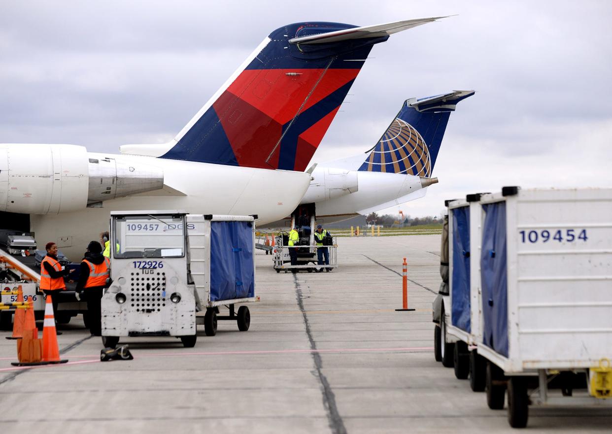 Luggage from a Delta Air Line flight is off-loaded in the foreground, while a United Airlines flight is loaded up before take off at the Lansing Capital Region International Airport.
