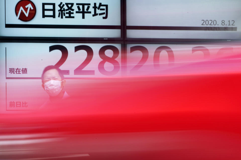 A man stands as a car drives by near an electronic stock board showing Japan's Nikkei 225 index at a securities firm in Tokyo Wednesday, Aug. 12, 2020. Shares were mostly lower in Asia on Wednesday after Wall Street pumped the brakes on its recent rally. (AP Photo/Eugene Hoshiko)