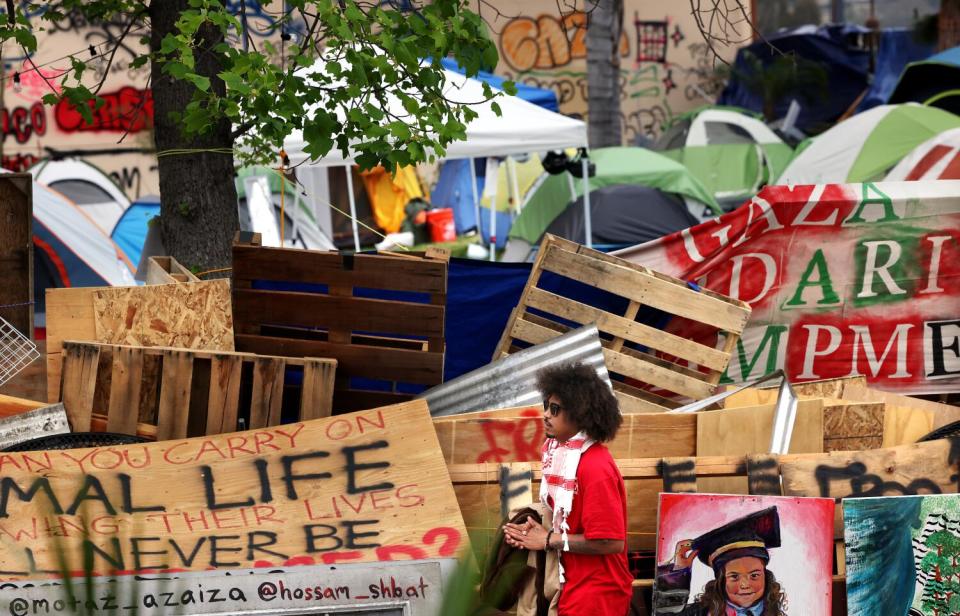 A young man in red walks past an encampment barricaded in plywood.