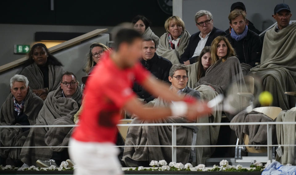 Spectaors wrapped in blankets watch as Serbia's Novak Djokovic plays a shot against Spain's Rafael Nadal during their quarterfinal match at the French Open tennis tournament in Roland Garros stadium in Paris, France, Wednesday, June 1, 2022. (AP Photo/Christophe Ena)