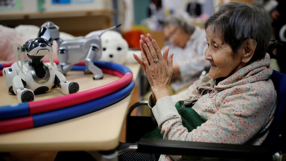 "Robo-companionship" options for people who are aging are gaining popularity in Japan, where <a href="https://www.cnn.com/2023/07/27/asia/japan-population-drop-2022-intl-hnk/index.html">there's a ballooning elderly population</a>. In this photo, taken in 2018, a nursing home resident in Tokyo claps to call a pet dog robot. - Kim Kyung-Hoon/Reuters