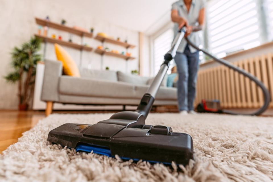Woman in jeans uses vacuum cleaner to clean beige rug. 