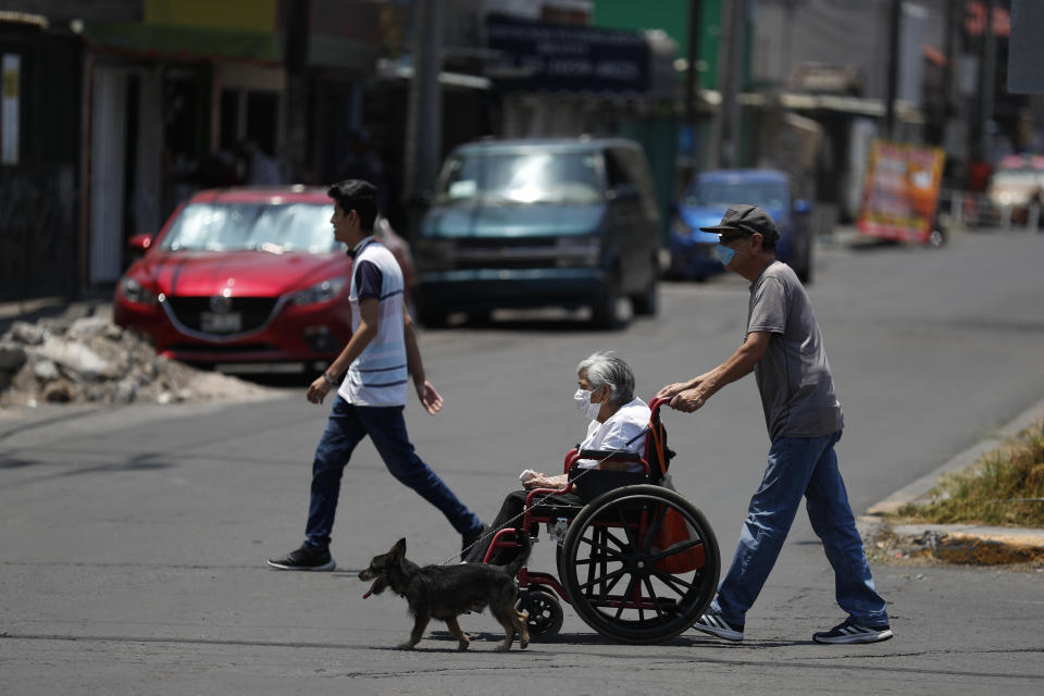 A man pushes a woman in a wheelchair as a dog walks alongside them, in the Iztapalapa district of Mexico City, Tuesday, May 5, 2020. Iztapalapa has the most confirmed cases of the new coronavirus within Mexico's densely populated capital, itself one of the hardest hit areas of the country, with thousands of confirmed cases and around 500 deaths.(AP Photo/Rebecca Blackwell)