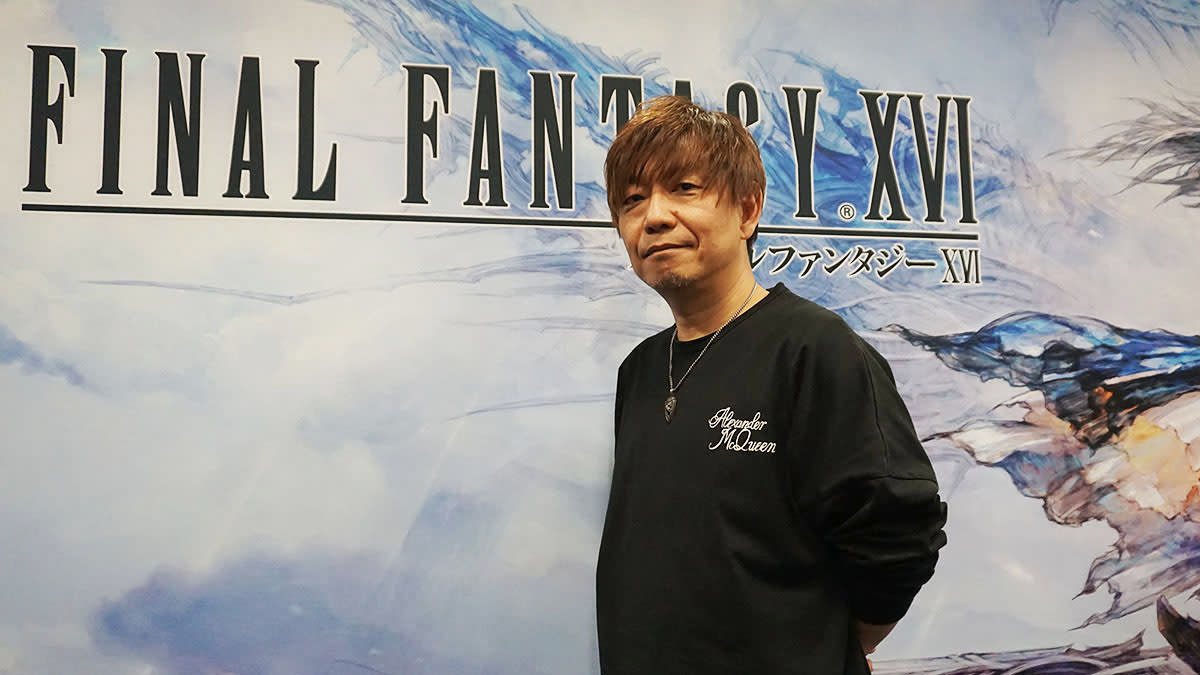  An image of Final Fantasy 16 producer Naoki Yoshida standing in front of a banner advertising the game. 