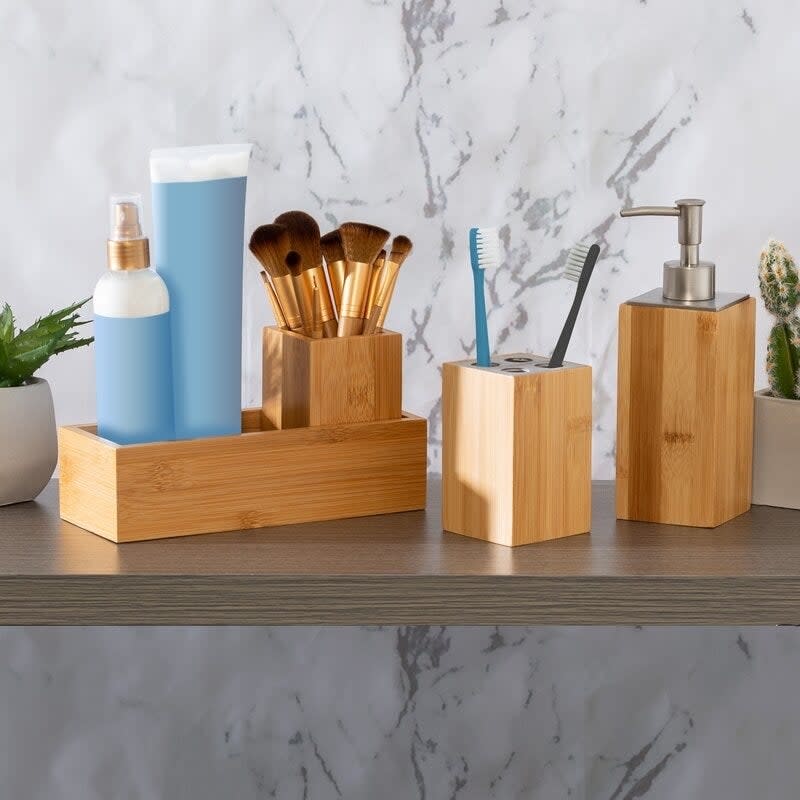 bamboo bathroom accessory set on a shelf, including a toothbrush holder, rectangular tray, accessory tray, and pump dispenser