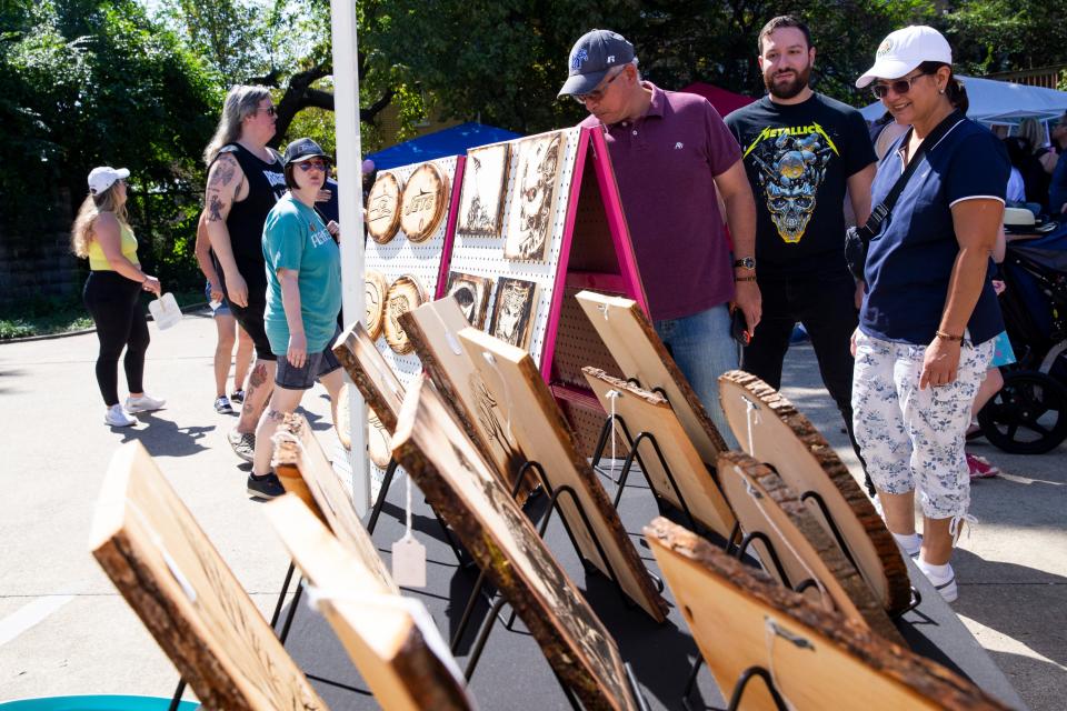 Attendees look at the artwork of Heath Augustine at his Rested Soul Wood Burns booth during the Cooper-Young Festival in Midtown Memphis, on Saturday, September 16, 2023.