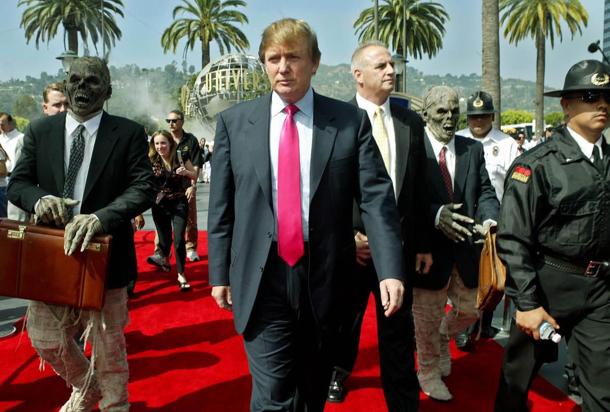 Donald Trump, center, arrives at Universal Studios Hollywood and is accompanied by persons dressed as mummies in business attire Friday, July 9, 2004 in Los Angeles. Trump is casting for 