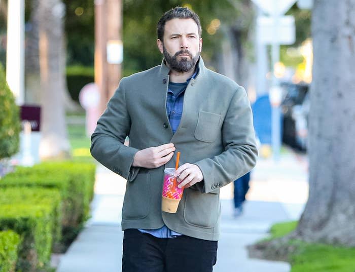 A closeup of Ben walking outside with coffee