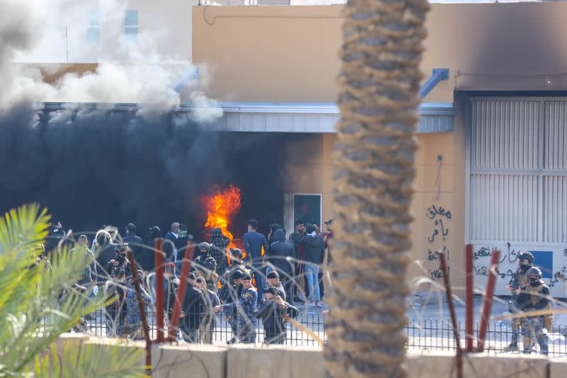 Attackers and assailants set fire to a gate as smoke rises from inside the compound of the U.S. embassy in Baghdad