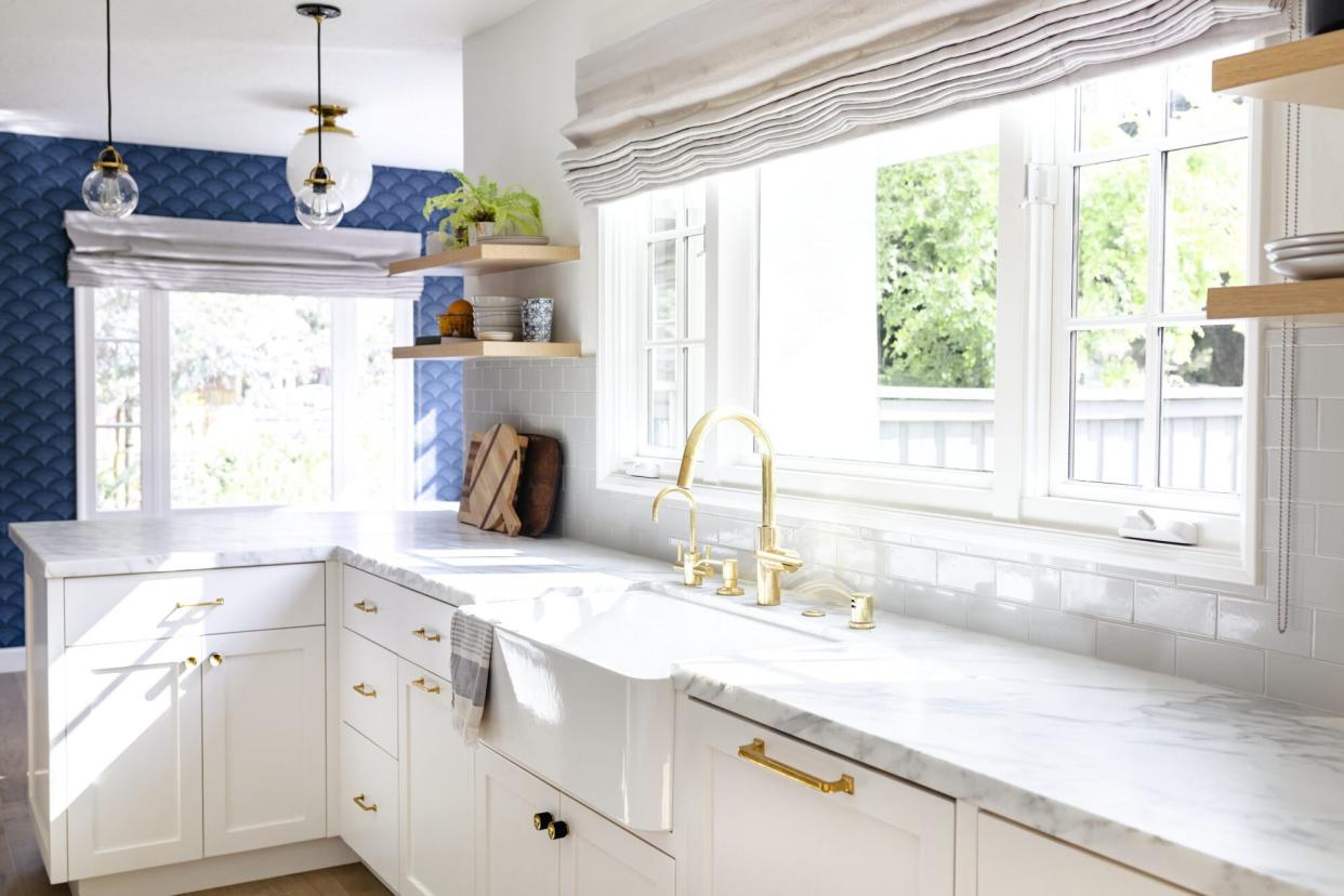 White kitchen with navy blue detailing and white marble counter with gold fixtures.