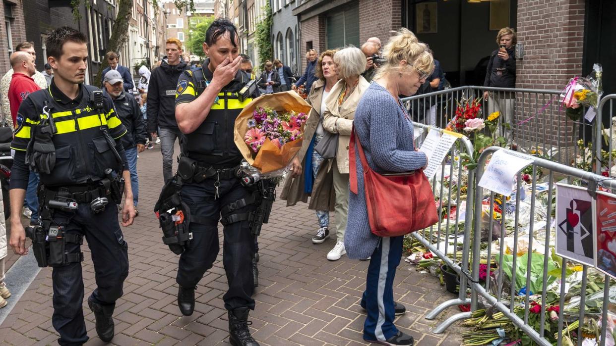 Polizisten bringen einen Blumenstrauß zu dem Blumenmeer für den Reporter Peter R. de Vries in der Leidswarsstraat.