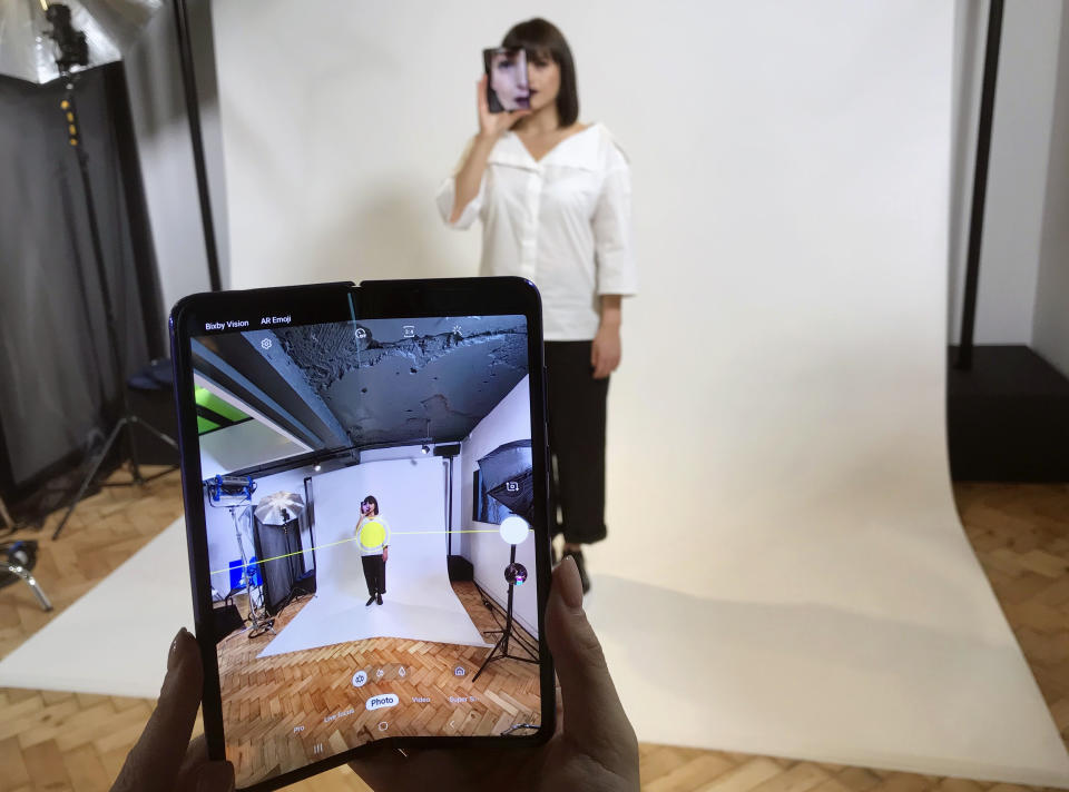 FILE - In this April 16, 2019, file photo, a model holds a Samsung Galaxy Fold smart phone to her face, during a media preview event in London. Samsung is pushing back this week's planned public launch of its highly anticipated folding phone after reports that reviewers' phones were breaking. The company had been planning to release the Galaxy Fold on Friday. Instead, it says it will to run more tests and announce a new launch date in the coming weeks. (AP Photo/Kelvin Chan, File)