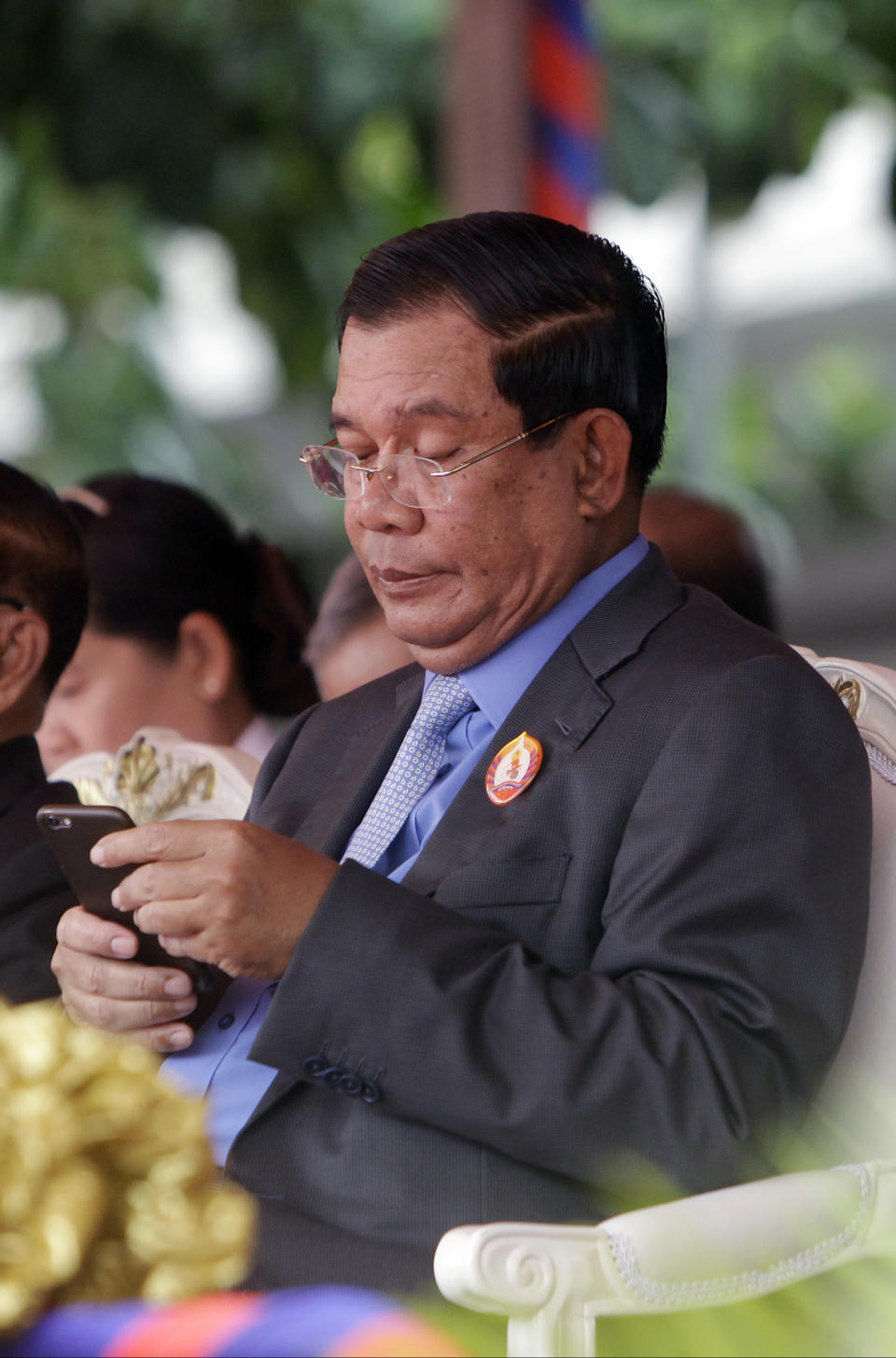 FILE - Cambodia's Prime Minister Hun Sen holds a mobile device during the celebrations of the 65th anniversary of the ruling Cambodian People 's Party in Phnom Penh, Cambodia, Tuesday, June 28, 2016. Cambodia’s Prime Minister Hun Sen, a devoted and very active user of Facebook, says he will no longer upload to the platform, and instead depend on the Telegram app for getting his message across. (AP Photo/Heng Sinith, File)