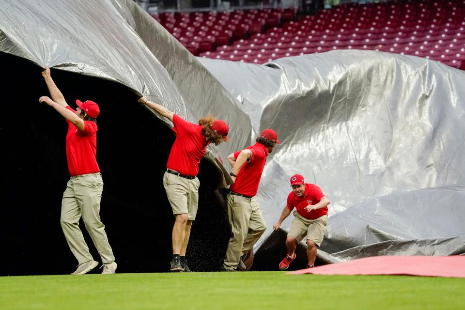 Cincinnati Reds grounds crewmen pull a rain tarp over the infield as rain moves in before a baseball game against the Philadelphia Phillies, Sunday, April 16, 2023, in Cincinnati.