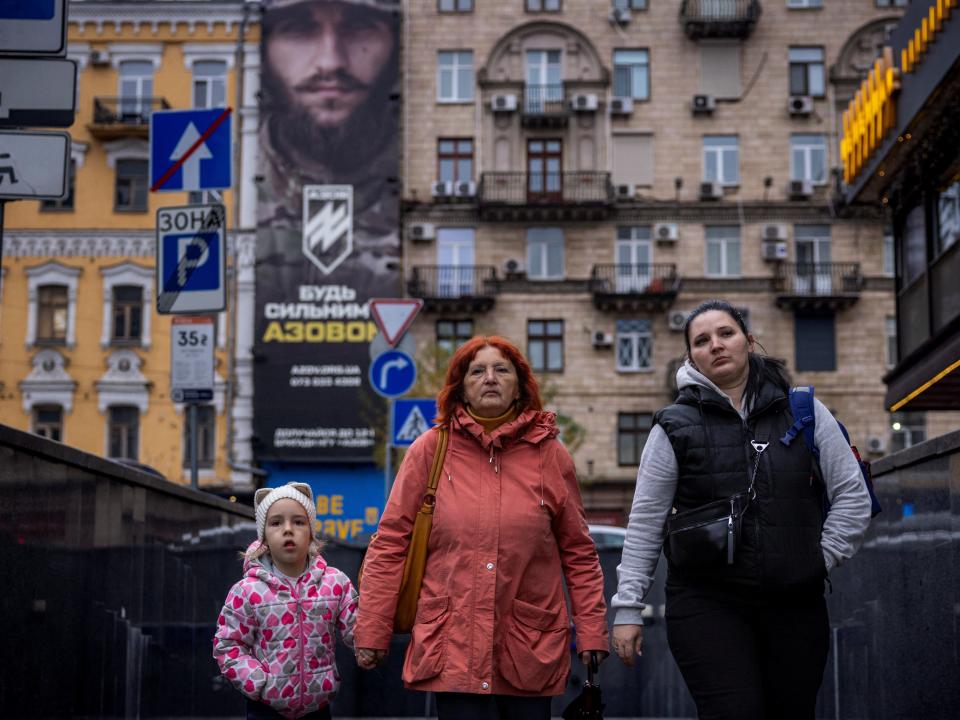 Women and a child walk near a recruitment poster for the Azov Assault Brigade of the National Guard of Ukraine in Kyiv (REUTERS)