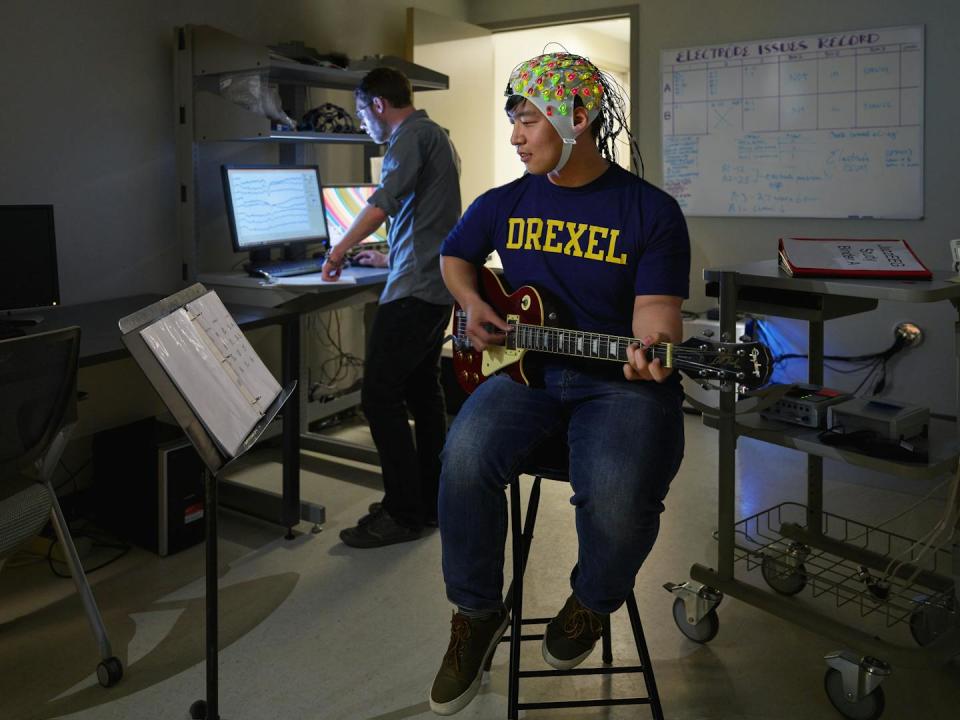 Молодой человек играет на гитаре в шлеме, покрытом электродами, измеряющими активность мозга