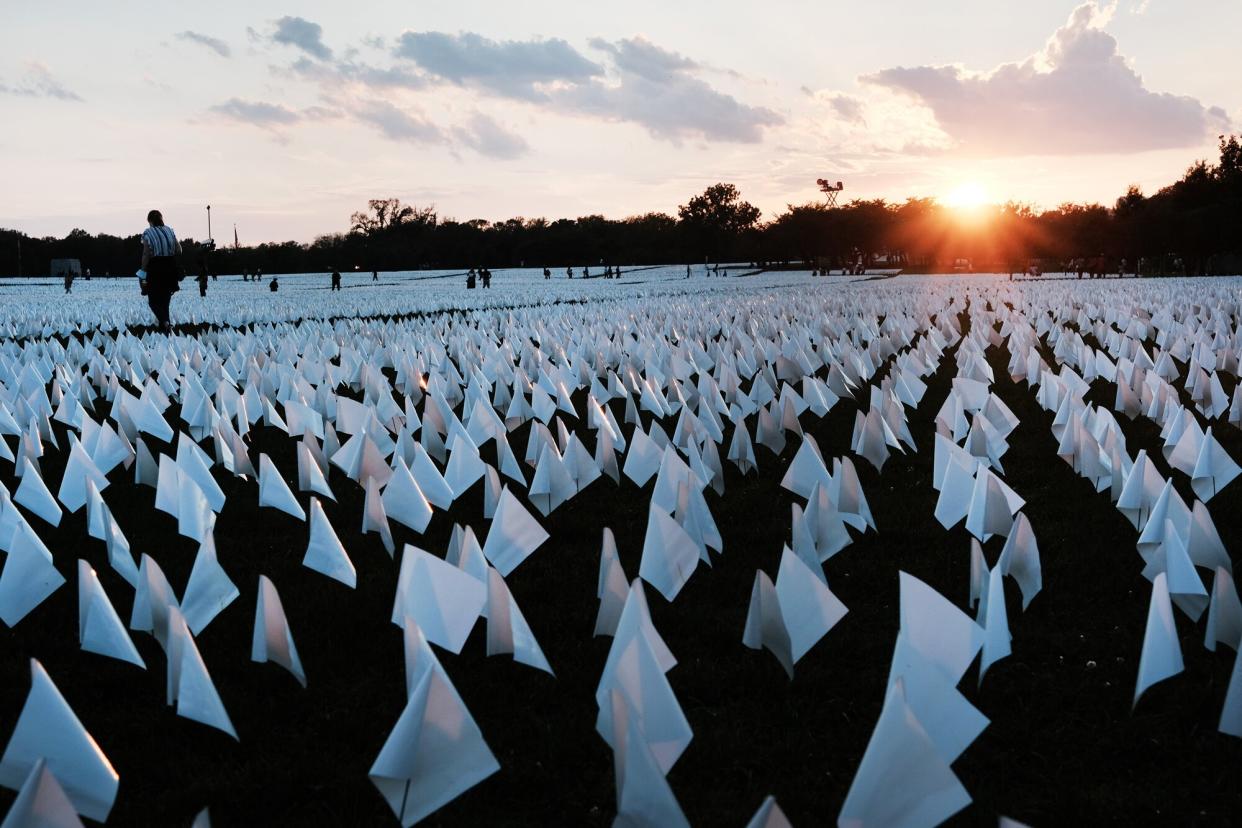 The sun sets as visitors walk through 'In America: Remember,' a public art installation commemorating all the Americans who have died due to COVID-19 near the Washington Monument on September 18, 2021 in Washington, DC. The concept of artist Suzanne Brennan Firstenberg, the installation includes more than 660,000 small plastic flags, some with personal messages to those who have died, planted in 20 acres of the National Mall.