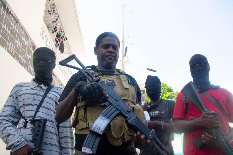 Gang leader Jimmy “Barbecue” Cherizier and his men, holding rifles, stand on a sidewalk.