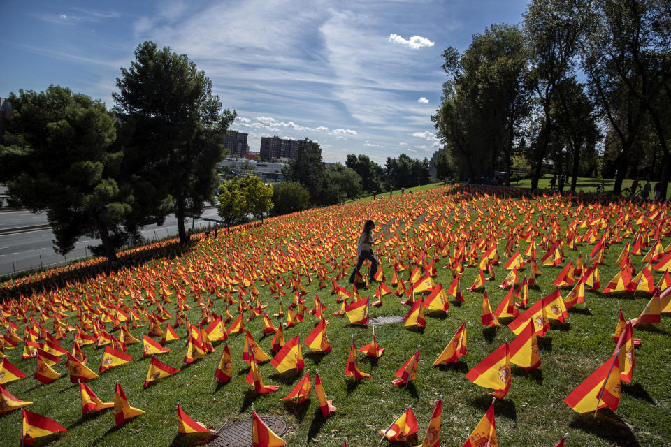 Una mujer camina entre decenas de banderas españolas colocadas en memoria de las víctimas de coronavirus, en Madrid, el 27 de septiembre de 2020. España alcanzó en octubre el millón de casos de coronavirus. (AP Foto/Manu Fernandez)