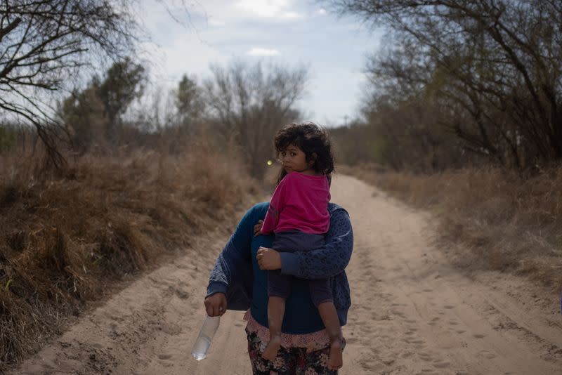 Migrant families walk down dirt road after crossing the Rio Grande River into thr U.S. from Mexico in Penitas, Texas