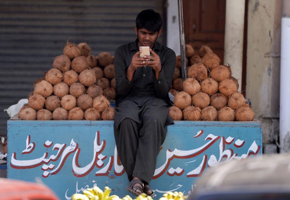 A Pakistani vendor uses his smartphone as he waits for customers at his stall at a market in Islamabad on October 11, 2018. (Photo by AAMIR QURESHI / AFP)        (Photo credit should read AAMIR QURESHI/AFP via Getty Images)