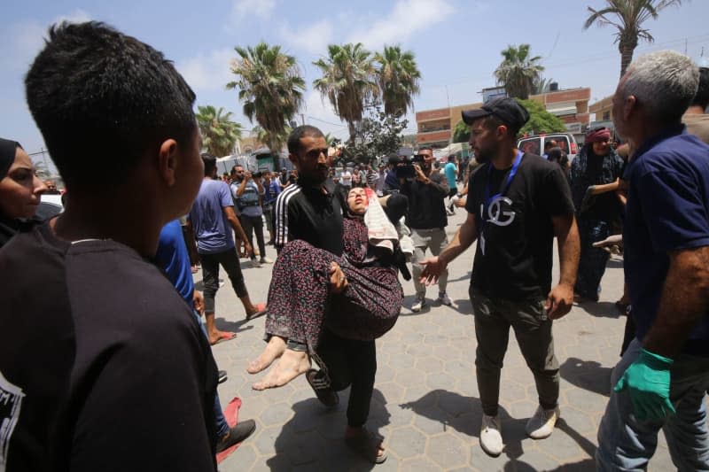 A Palestinian man carries an injured woman to Al-Aqsa Martyrs Hospital following simultaneous Israeli attacks on Nuseirat Refugee Camp, al-Bureij Refugee Camp and al-Maghazi Refugee Camp. Israeli special forces rescued four hostages in broad daylight on Saturday from the Nuseirat refugee district in the centre of the Gaza Strip after 246 days in captivity, the army said. Omar Naaman/dpa