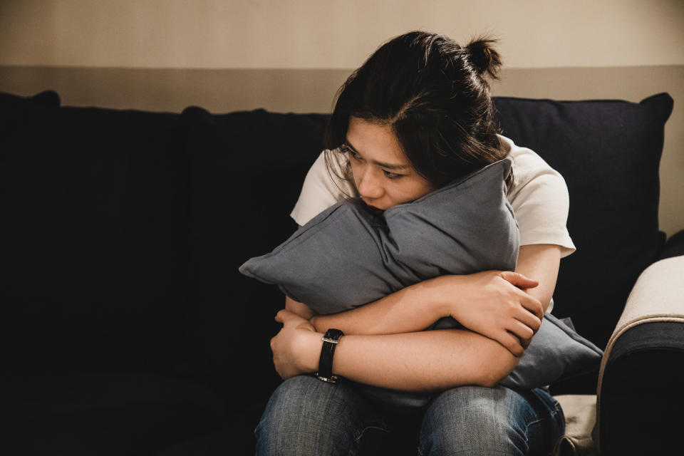 Someone sits on a couch, hugging a pillow, looking like they're on the verge of tears