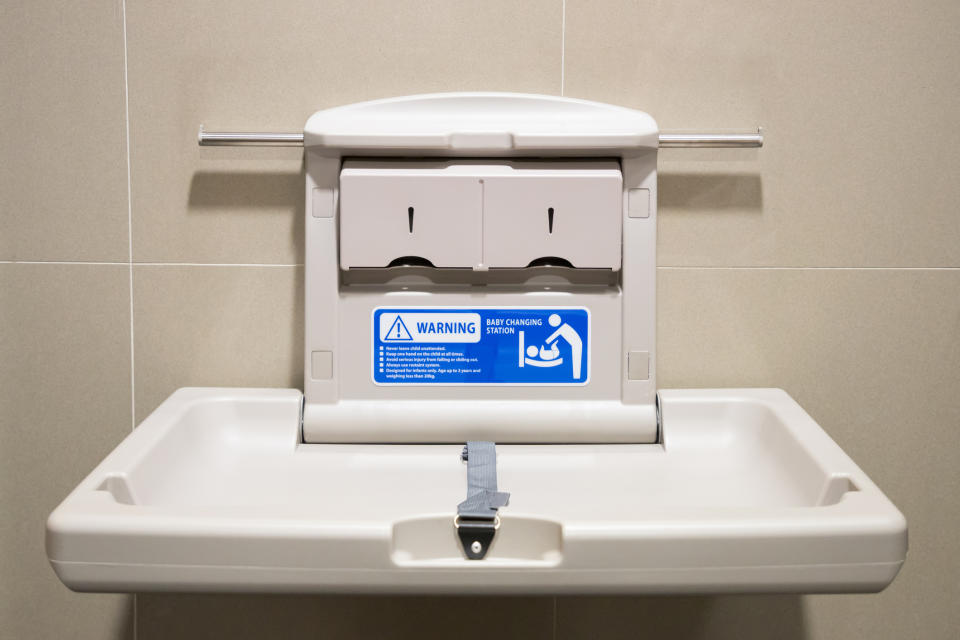 Baby changing station with safety instructions, mounted on a restroom wall