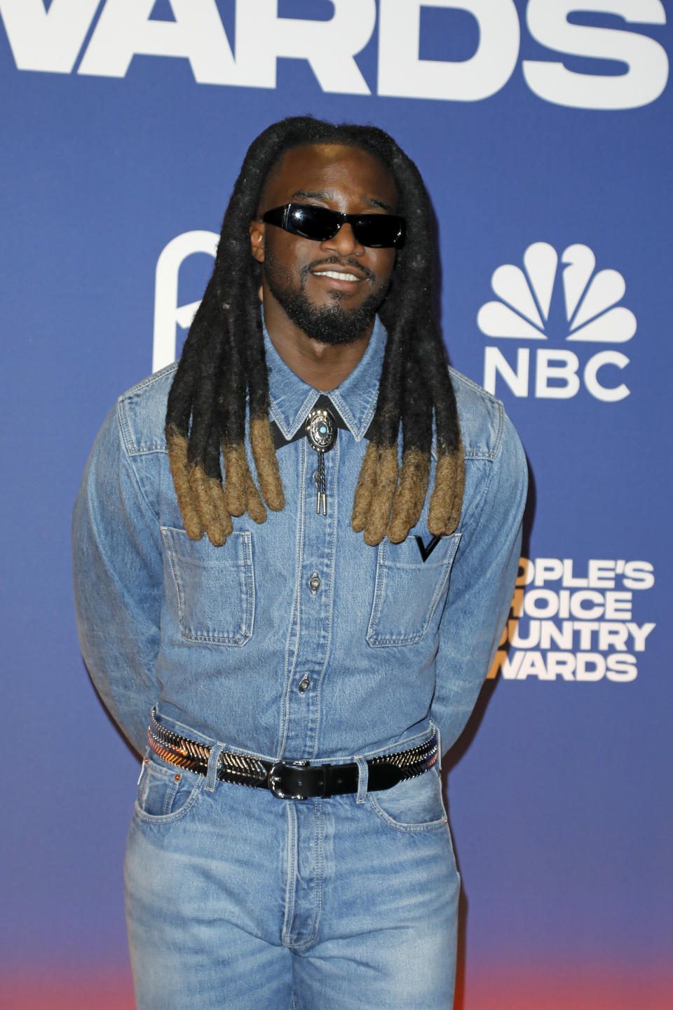 I don't know who it is. Person on the red carpet wearing denim outfit, sunglasses and decorative belt. BNC and "People's Choice Country Award" the logos are visible