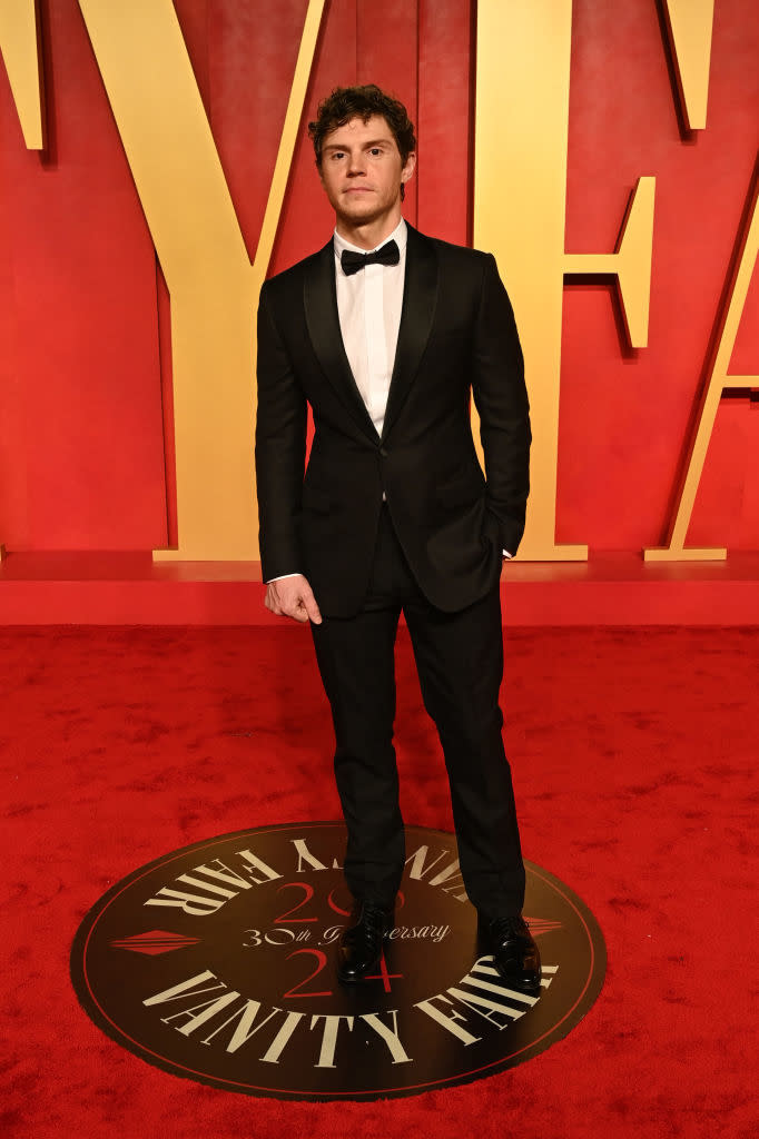 Man in a black suit and bow tie standing on a Vanity Fair event logo