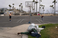 People play basketball as a homeless man sleeps near the court in the Venice neighborhood of Los Angeles, Tuesday, June 29, 2021. (AP Photo/Jae C. Hong)