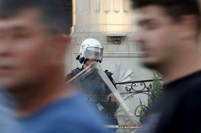 People walk past a police officer guarding the foreign ministry building, during a protest in Skopje, North Macedonia, on Wednesday, July 6, 2022. Thousands of people were marching the fifth night of protests in North Macedonia's capital after French President Emmanuel Macron last week announced the proposal, which many in the small Balkan country find controversial. (AP Photo/Boris Grdanoski)