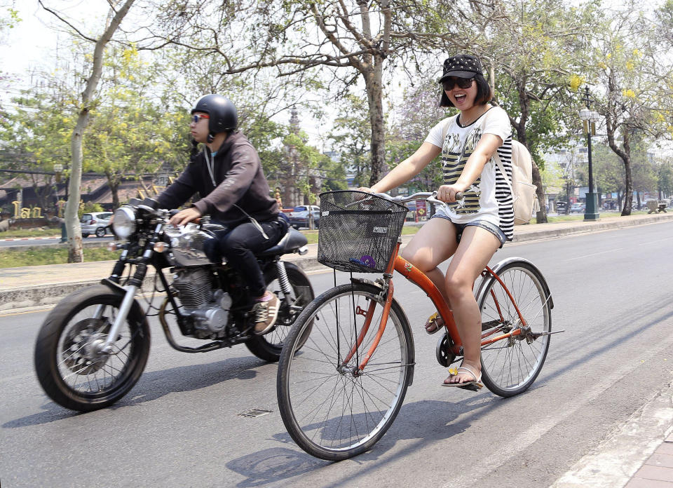 In this March 30, 2014 photo, a Chinese tourist rides on a bicycle during a tour in downtown Chiang Mai province, northern Thailand. The bucolic, once laid-back, campus of one of Thailand’s top universities seems to be under a security clampdown these days. Not against a terrorist threat, but Chinese tourists, thousands of them, who have clambered aboard student buses, eaten in cafeterias, sneaked into classes to attend lectures and even pitched a tent by a picturesque lake. Now visitors are restricted to entering through a single gate manned by Mandarin-speaking volunteers who direct Chinese tourists to a line of vehicles for guided tours. (AP Photo/Apichart Weerawong)