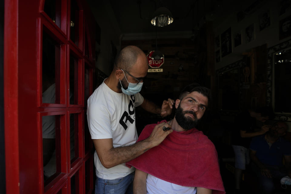 A Lebanese barber shaves the beard of a customer at the door of his shop during a power outage in a southern suburb of Beirut, Lebanon, Wednesday, Aug. 11, 2021. Lebanon, which is mired in multiple crises including a devastating economic crisis, has faced months of severe fuel shortages that have prompted long lines at gas stations and plunged the small country, dependent on private generators for power, into long hours of darkness. (AP Photo/Hassan Ammar)