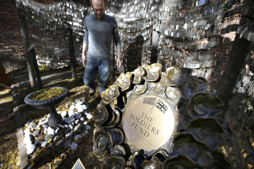 In this Wednesday, Nov. 7, 2018 photo Tim Wenrich, of Boston, caretaker at Old North Church, stands near a bronze wreath, right, that is part of a memorial that honors fallen soldiers from the U.S. and Britain, on the grounds of the church in Boston. Since 2005, thousands of military dog tags have hung like wind chimes outside the church in touching tribute to American forces killed in Iraq and Afghanistan. The new plaque and wreath will explain the meaning of the dog tags and acknowledge Britain's contribution and sacrifice. (AP Photo/Steven Senne)