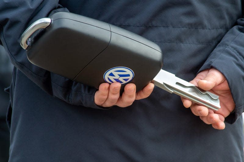 A man is holding an oversized key with a Volkswagen symbol in his hands. The key was part of a symbolic exchange.