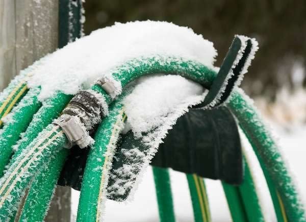 Green garden hose on a hose holder, covered in snow.