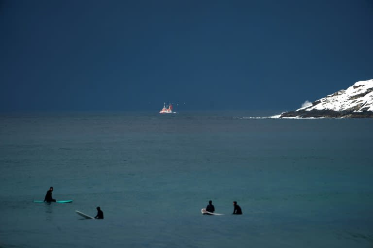 Surfers wait for waves as a fishing boat sails by off the Lofoten islands, within the Arctic Circle